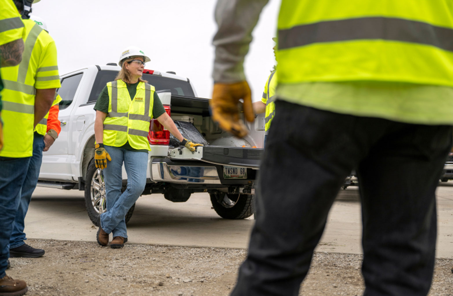 An NG Gilbert crew member leans on a truck bed in discussion with another team member, who stands in the foreground.