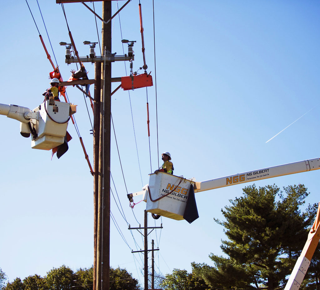 Two NG Gilbert crew members stand in cherry pickers to tend to a power line.