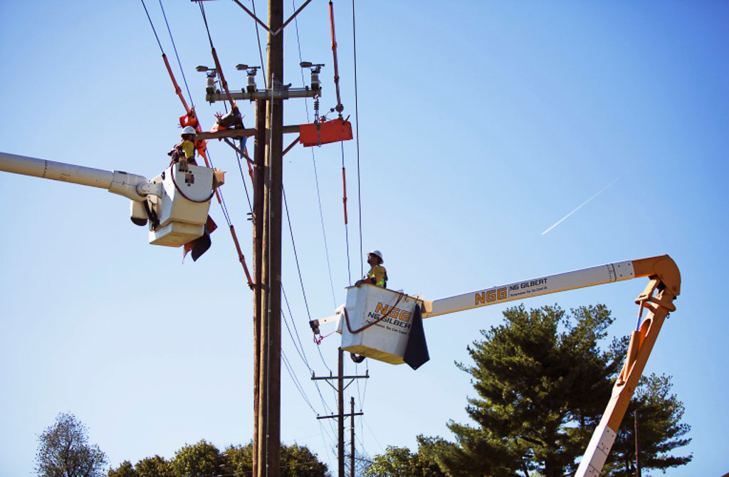 Two NG Gilbert crew members stand in cherry pickers to tend to a power line.