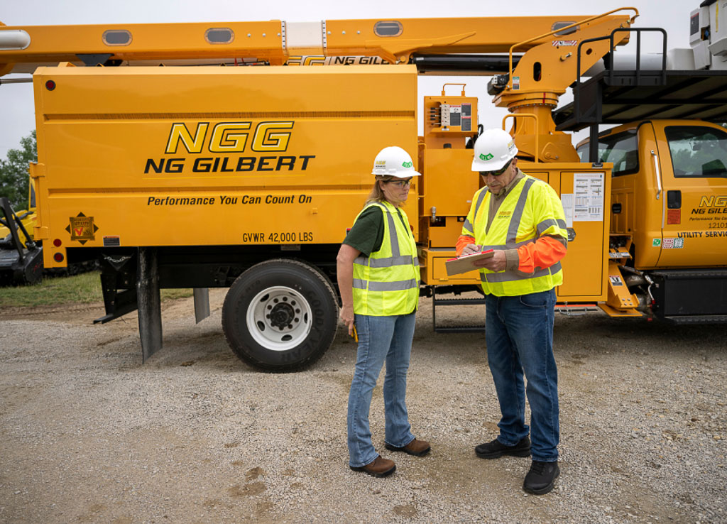 Two NG Gilbert team members wearing hard hats and safety vests discuss in front of an NG Gilbert truck