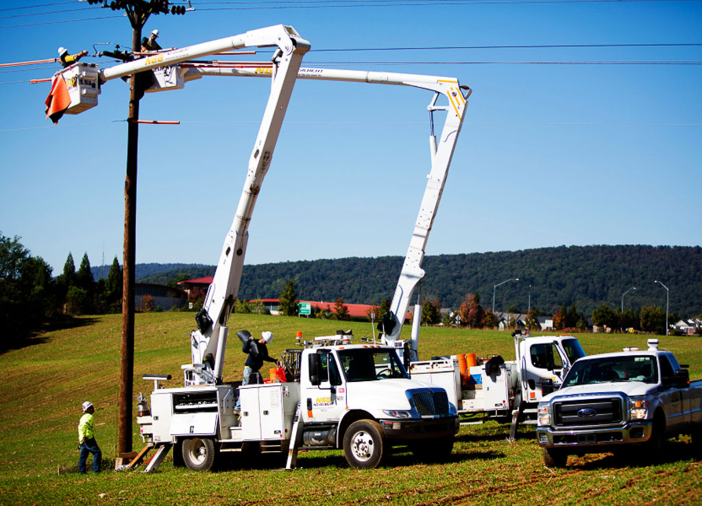 Two NG Gilbert cherry picker trucks holds several crew members as they lift two workers to work on an overhead line.