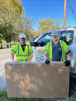 Two men standing behind a large box with a truck in the background