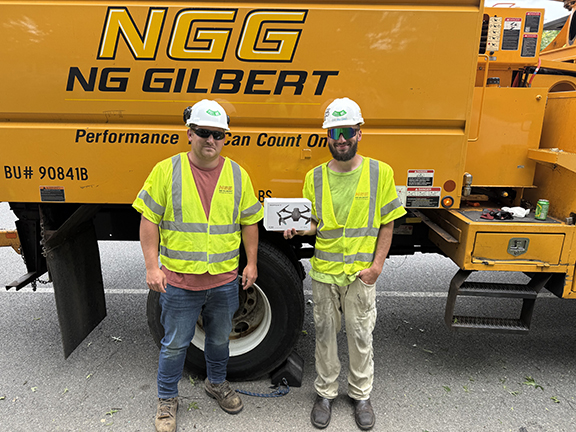 Two men standing next to a yellow truck with one man holding a drone.