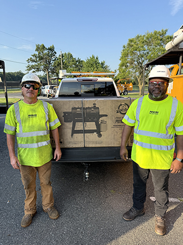 Two men standing by a truck with a grill in between them.