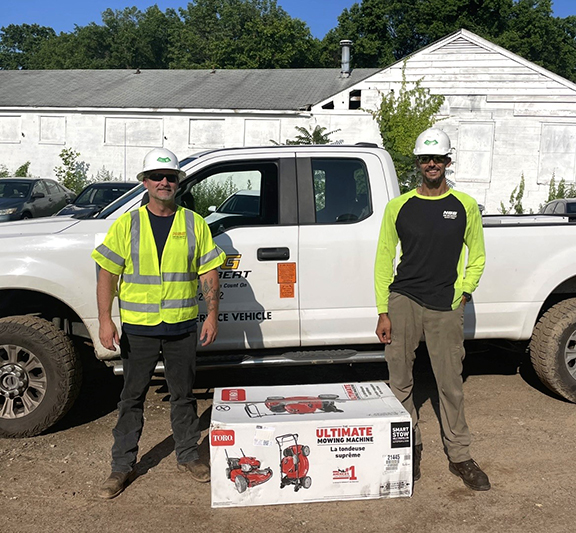 Two men standing near a truck with a lawnmower in a box between them.